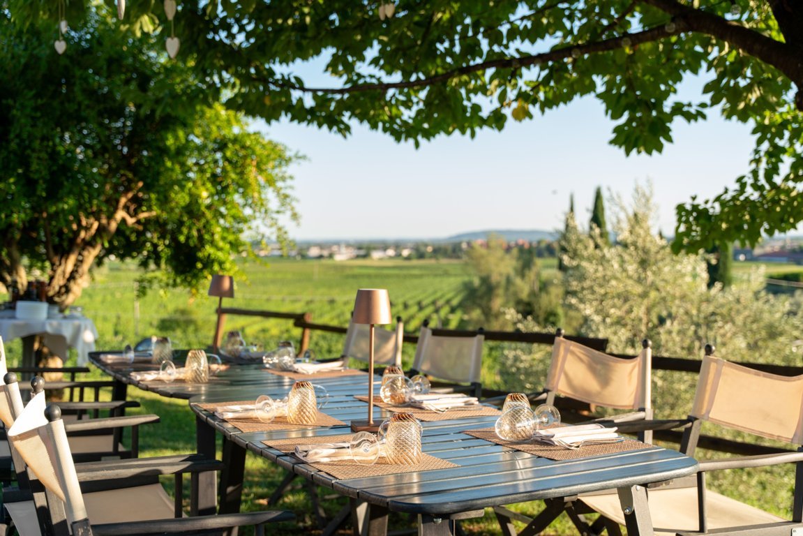 Il giardino dell’Osteria Solder, con tavoli imbanditi all’ombra degli alberi e lo sguardo che si perde tra i vigneti. Un’atmosfera di pace e convivialità, dove natura e sapori si incontrano in un’esperienza autentica.